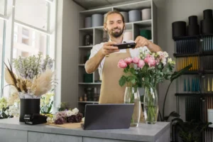 Attractive young male florist make bouquet and taking photo on smart phone for social media