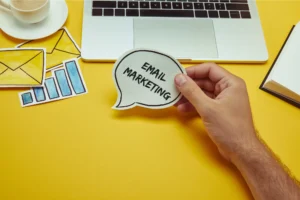 Cropped image of man holding speech bubble with email marketing lettering near laptop